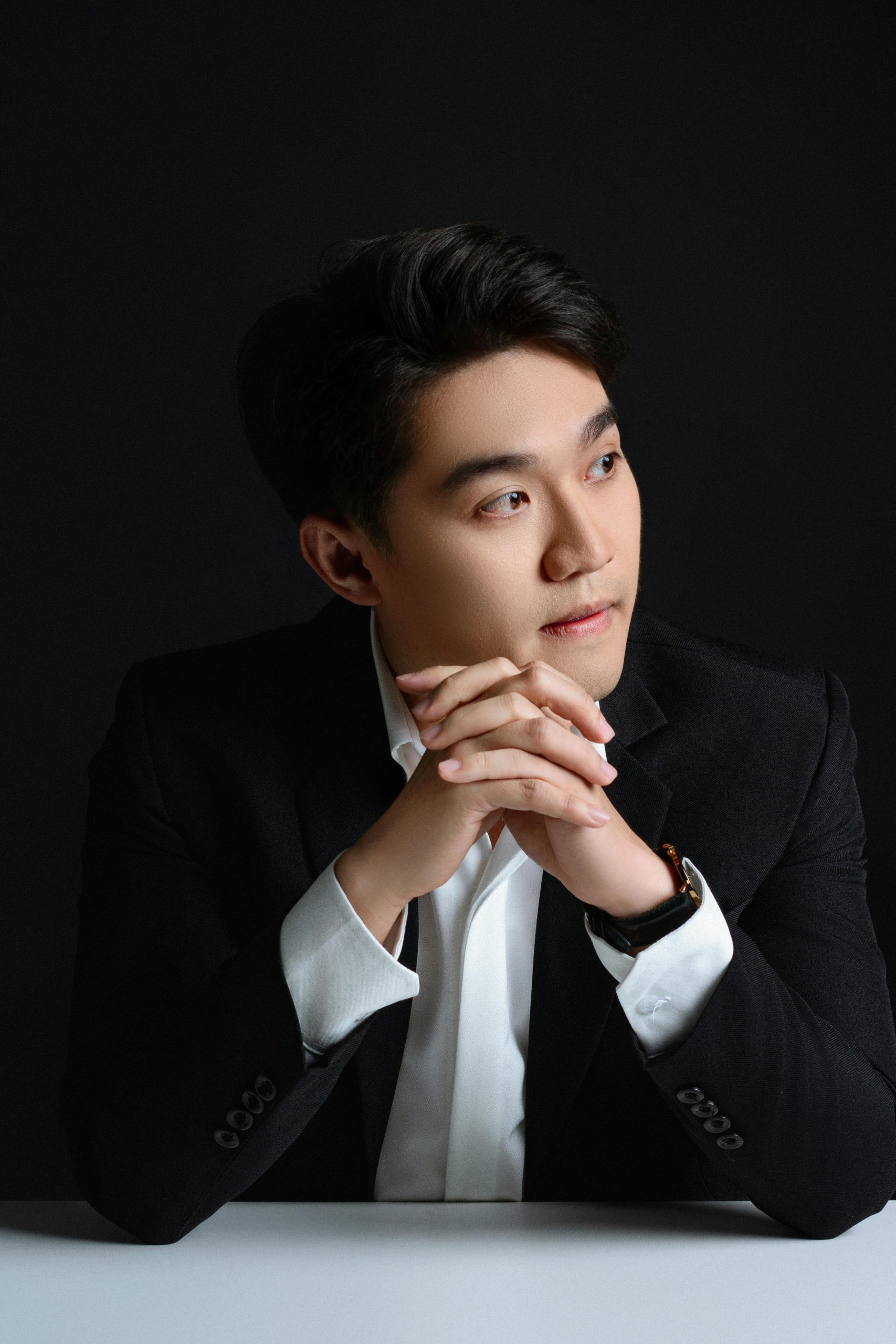 Studio portrait of a confident businessman in a black suit with hands clasped thoughtfully.