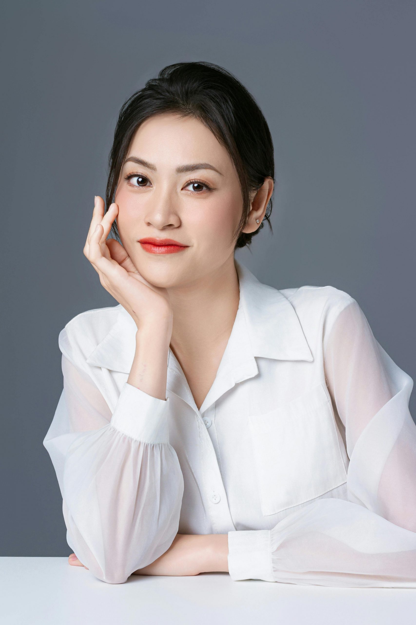 Portrait of an elegant Asian woman in a white shirt with a thoughtful pose.